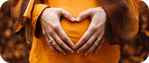 close up of woman's hands forming a heart over her pregnant belly